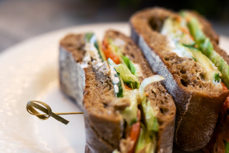Rustic multigrain sandwich halves on plate, closeup shot showing sliced brown bread filled with...