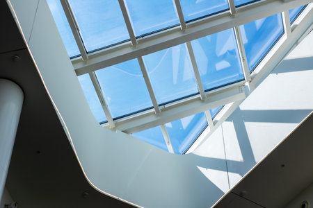 bright glass skylight viewed from interior, triangular panes forming geometric grid against clear...