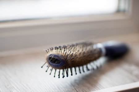 worn brush on windowsill after styling, closeup showing tangled bristles and strands, soft morning...