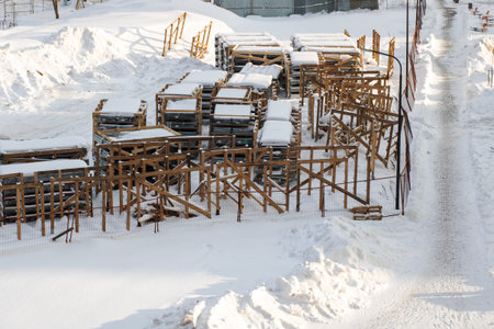 snow covered wooden scaffolding stacked outdoors on industrial lot after heavy snowfall, rows of...