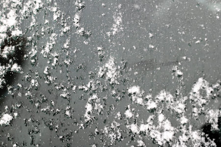 Dark asphalt with scattered salt flakes, closeup view of gritty winter residue on road surface,...