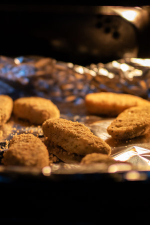 breaded chicken nuggets baking in oven, warm golden light on foillined tray, breadcrumbs crisping...