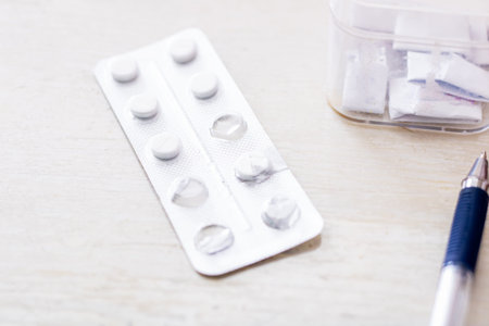 blister pack pills on wooden table, clear plastic container and pen nearby, empty foil cavities and...