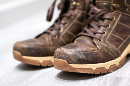 worn brown hiking boots on floor, scuffed leather and tan lug soles, laces loosely tied, sidebyside...