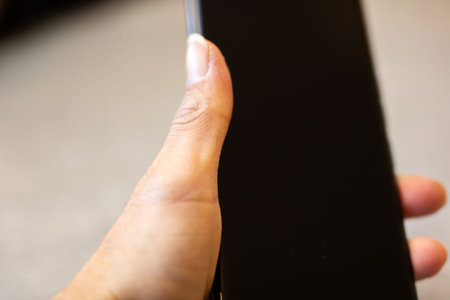 Closeup hand holding phone screen, softfocus neutral background, thumb near edge, slight glare on...