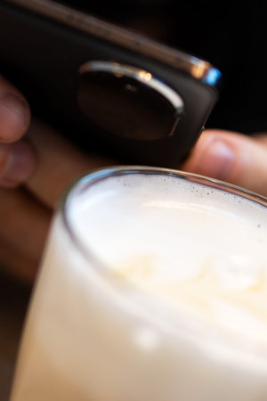 Closeup hand holding device above glass, cream foam visible, testing near beverage, warm ambient...