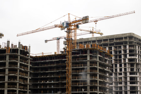 Multiple tower cranes above skeletal highrise structures, concrete cores rising as cranes lift...