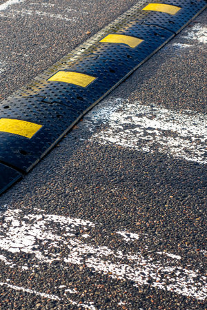 Yellow speed bump across worn asphalt, rubber ridge with bright paint blocks sitting beside faded...