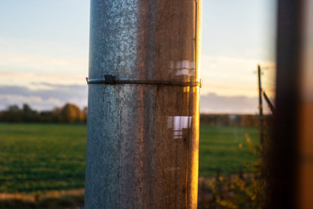 Metal pole closeup golden hour field. Weathered galvanized surface catching warm light, subtle rust...