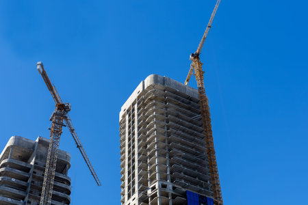 Tower construction with cranes blue sky. Skeletal concrete cores rise above scaffolding and steel...