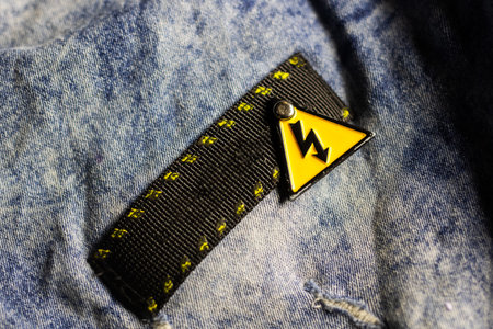 Yellow warning tag on denim, closeup showing black stitched loop with lightning symbol, textured...