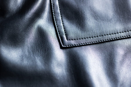 Black leather pocket closeup showing subtle grain and precise stitching, glossy finish reflecting...