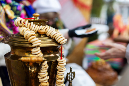 Brass samovar draped with bagels, vendor stall at outdoor market, colorful textiles in background,...