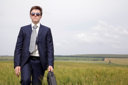Businessman in a suit goes along the field thinking about workの写真素材