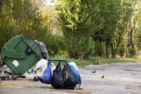 homeless hunger makes feed on from the container with garbage