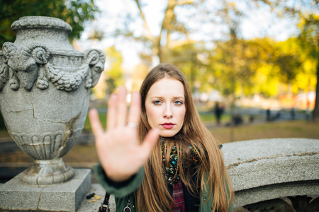 Attractive young woman in park is displeased and making a stop sign with her handsの写真素材