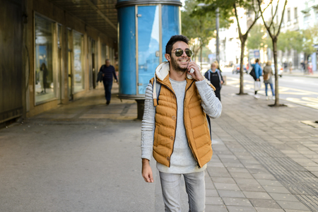 Young hipster with orange jacket and sunglasses with his smart phone in the city streetの写真素材