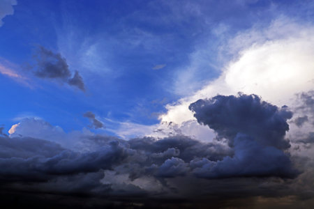 Dark, towering storm clouds billow across a deep blue sky, illuminated by soft light that creates a...