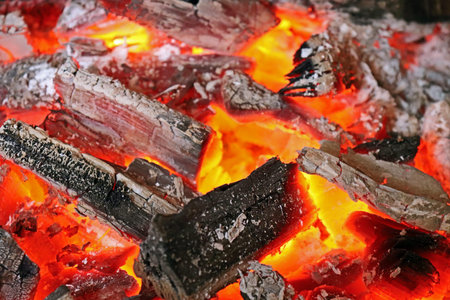 Close-up of glowing charcoal embers and partially burned wood, with intense orange heat radiating...