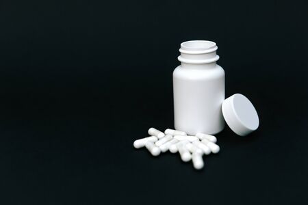 White jar with pills on a darck background.