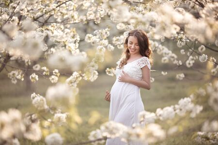 Beautiful pregnant woman walks outside in blooming garden.