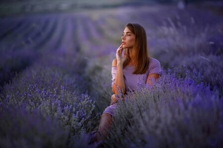 Summer portrait of a beautiful girl with long hair. woman with sexy figure. European girl in lavander field.Golden Fashion Girl Portrait. Short purple dress. Sunset.の写真素材