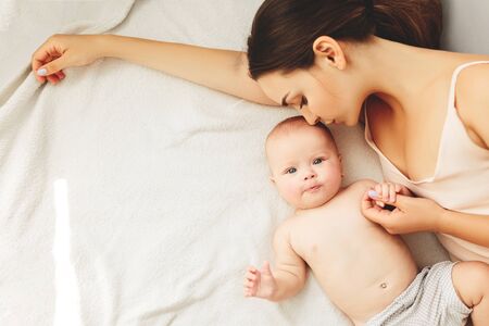 Young beautiful mother lies with the baby on the bed, gently kisses, sleeping together.