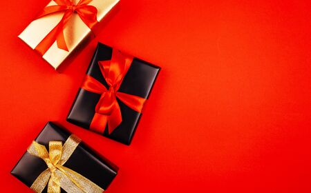 Christmas gifts with ribbon bow on a red background, black, goldの写真素材
