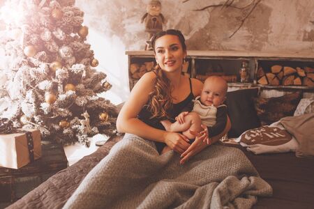 Smiling mother playing with lovely baby near Christmas treeの写真素材