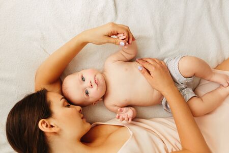 Young beautiful mother lies with the baby on the bed, gently kisses, sleeping together.