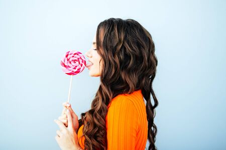 Woman licking a red shiny lollipop. Close up against white background.の写真素材