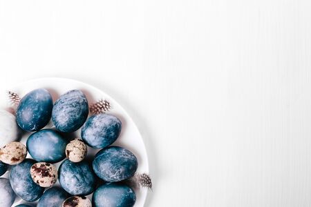 Beautiful group ombre blue Easter eggs with quail eggs and feathers on a white wooden background....