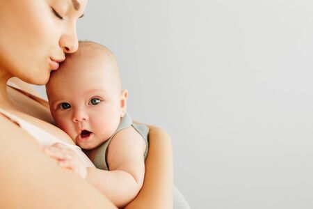 A little baby girl smiles and plays on the bed with her mom, dressed in knitted sweaters pastel fashionable shades, in a room, cozy house, modern design. Happy Family at home, concept of motherhoodの写真素材