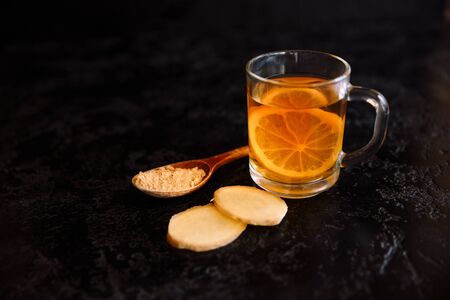 A composition of ginger roots and a spoon of milled ginger on a dark background