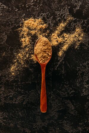 A composition of ginger roots and a spoon of milled ginger on a dark background