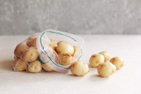 Potatoes in textile grocery mesh bags. Fruits and vegetables in reusable eco friendly packaging on white background. Zero waste shopping, plastic free, stop pollution, ecological concept.の写真素材