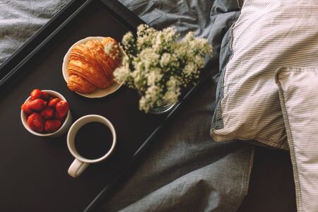 Breakfast on a tray in bed at home white dark linen. croissant tea strawberries.の写真素材