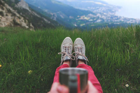 Closeup photo of cup with tea in travelers hand over out of focus mountains view. A young tourist...