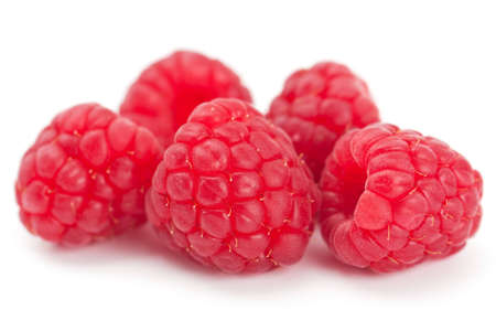 Studio closeup on white of five luscious ripe red juicy fresh raspberries with shallow depth of...