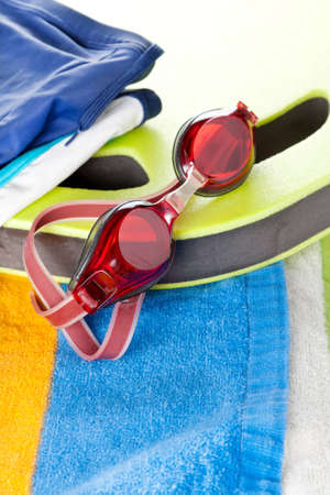 Colourful beach towel with a pair of protective red swimming goggles resting on the edge of a board in a leisure and sport conceptの写真素材