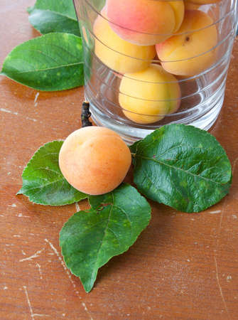 Fresh apricot lying on three leaves on a scratched grungy brown rustic tabletop alongside a jar containing additional fruitの写真素材