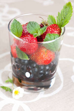 Whole fresh juicy ripe blackberries and strawberries in a transparent glass topped with green mint leavesの写真素材