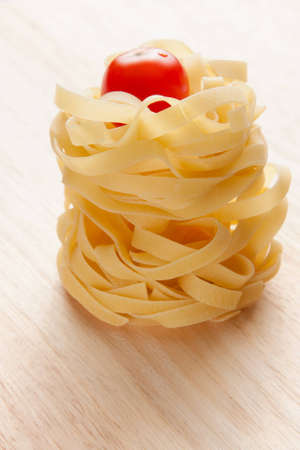 Stacked uncooked Italian pasta and fresh ripe red tomato ready to be used in the kitchen for Mediterranean cuisineの写真素材