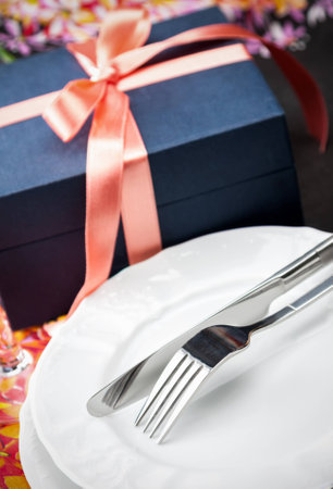 Simple stylish white dinner plates and cutlery with a gift box tied with a decorative red bow, high angle closeup shotの写真素材