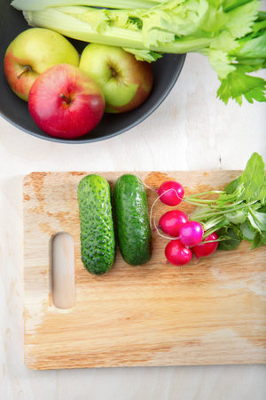 Fresh vegetables in the kitchen with a high angle view of a bowl containing fresh apples and celery alongside a chopping board with radish and cucumber for making a fresh vegetarian saladの写真素材