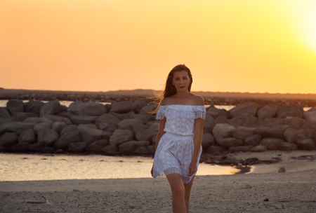 Girl in white dress at the beach during sunsetの写真素材