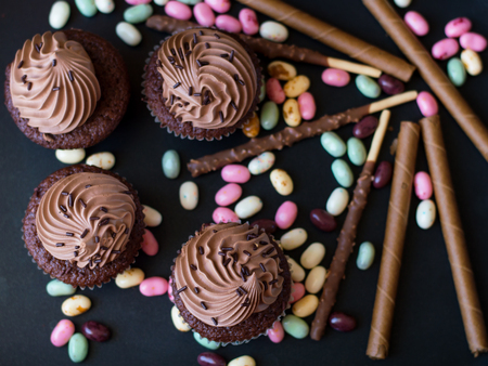Small chocolate cupcakes and a lot of jelly sweets and chocolate sticks on black background