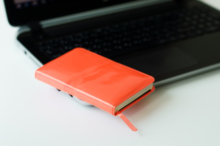 Red paper notebook on black computer. Small business diary and laptop on white office table. Business conceptの写真素材