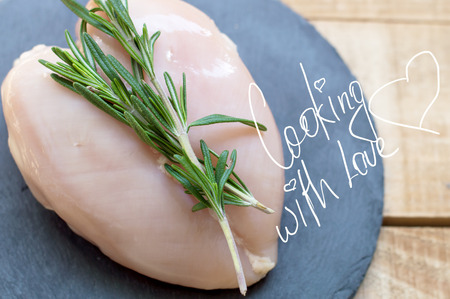 Heart-shaped chicken breast decorated with fresh green rosemary. Raw chicken fillet on black slate plate. Cooking conceptの写真素材