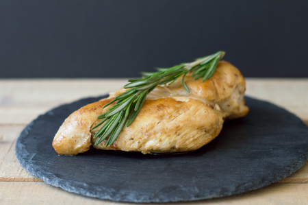 Fried chicken breast with fresh rosemary on small slate board on wooden table, black backgroundの写真素材